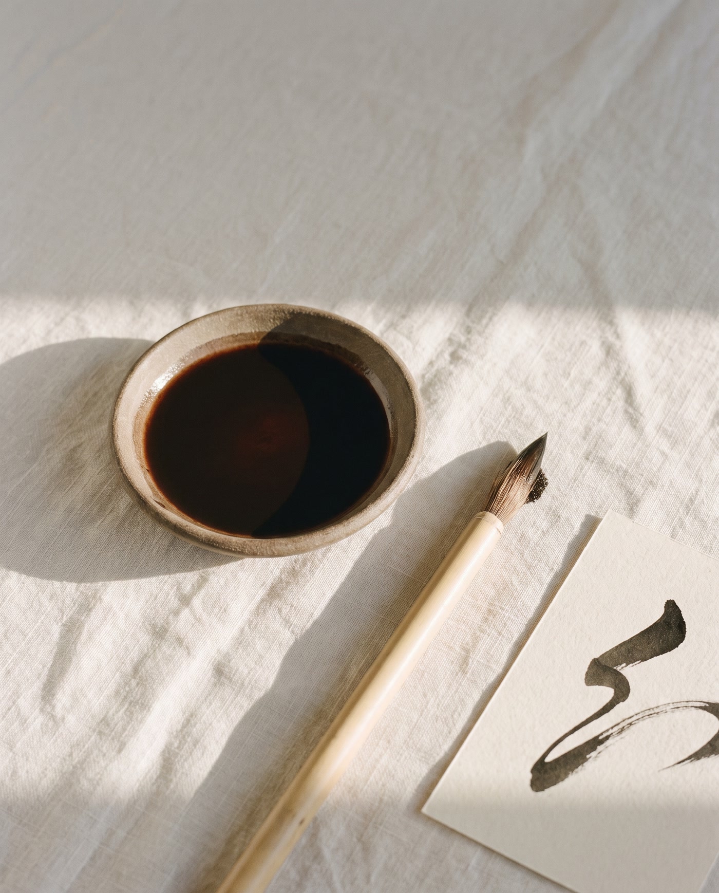 A brush lifted from a bowl of ink beside a page carrying a single hand-drawn stroke.