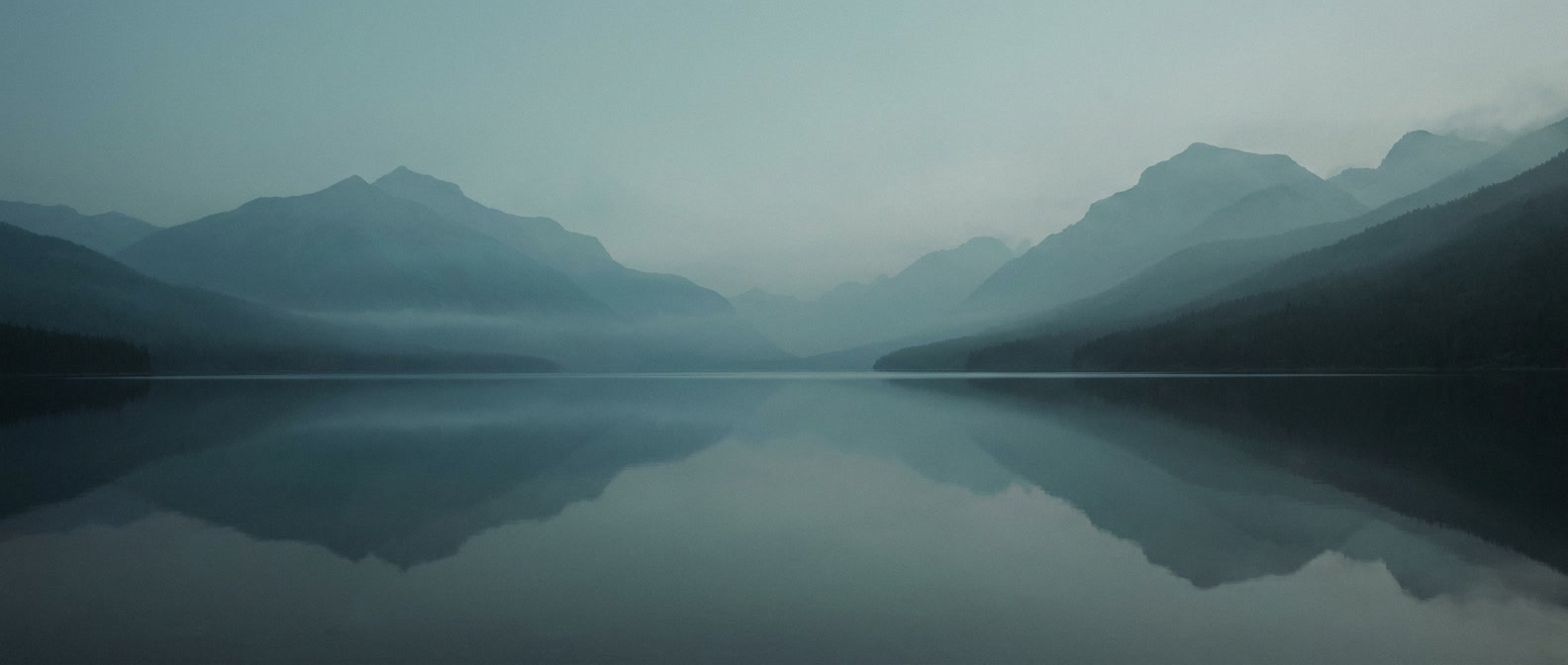 Misty layered mountain ridges over still water, a metaphor for infrastructure beneath the surface.